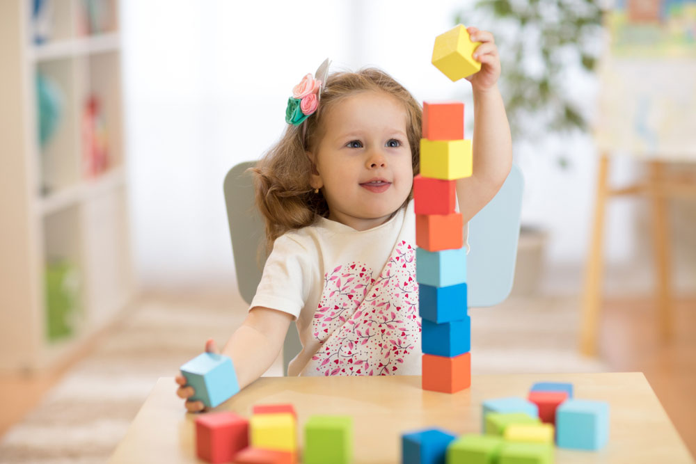 Cute child stacks building cubes sitting at table