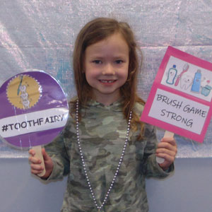 little girl holding dental banner and smiling